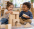 Two toddlers working together to build a wooden block tower in a bright child care classroom.